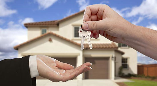 image of one hand dropping a set of keys into another hand with house in the background