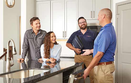 man and woman sitting at kitchen counter smiling with two David Weekley Homes Team Members