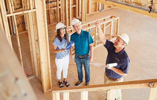 man and and two men wearing hard hats inspecting a home that has been framed