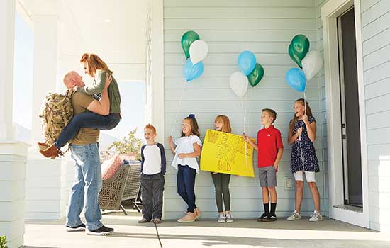 image of military homecoming on front porch with children holding up a sign that says welcome home dad