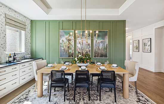 This David Weekley model home’s dining space features a soft green board and batten take on the classic shiplap interior wall concept and features a mix of wood and metal furniture to accentuate the theme.