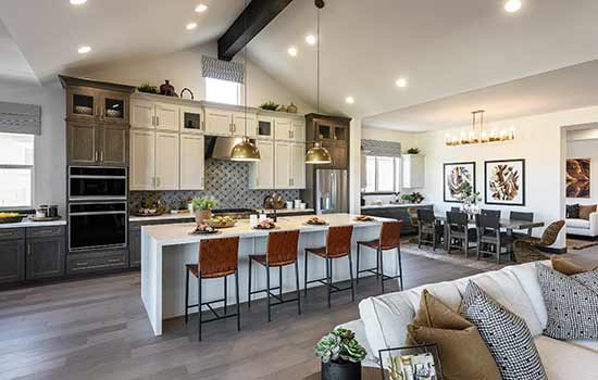 This David Weekley model home’s kitchen features mixed cabinetry, a patterned tile backsplash, rustic industrial finishes, and an exposed wood beam at the ceiling to bring together the modern farmhouse style.