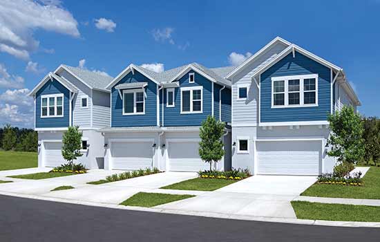 The front of four, two-sotry townhomes, each with a forward-facing garage and driveway, with light landscaping between the driveways, and sharing a color scheme of soft whites and blues at the upper level.