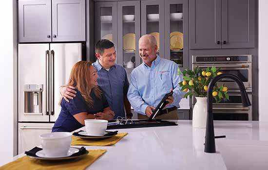 Two Homebuyers and a David Weekley Homes Team Member speak while referencing details on a tablet while spending time in a beautifully appointed model home’s kitchen.