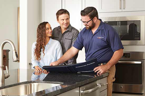 pman and woman in kitchen with man showing them information inside a notebook