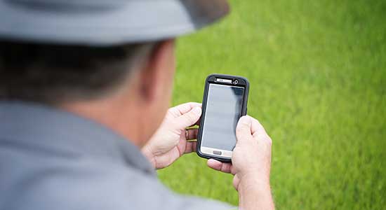 man wearing hard hat looking at cellular phone in his hand
