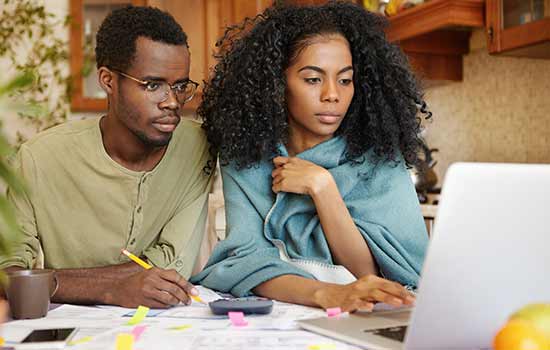 a man and a woman sitting at a table with papers and both are looking at a laptop screen