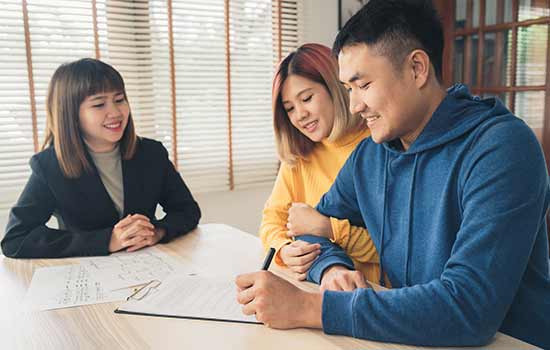 three people sitting at table looking at papers and man is signing papers.