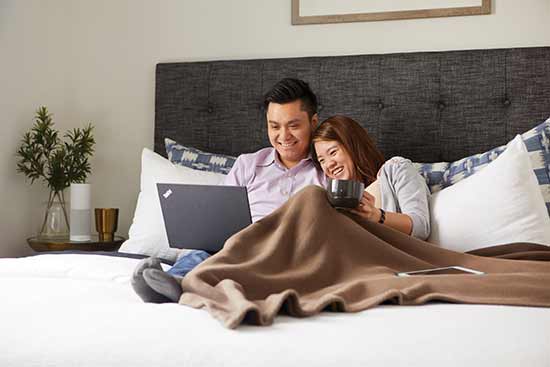 man and woman in bed looking at laptop