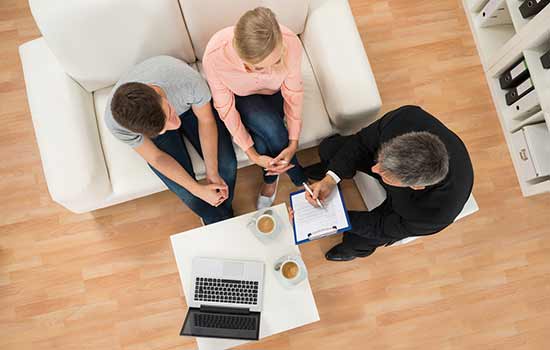 3 people sitting in chairs looking at a laptop open on the coffee table