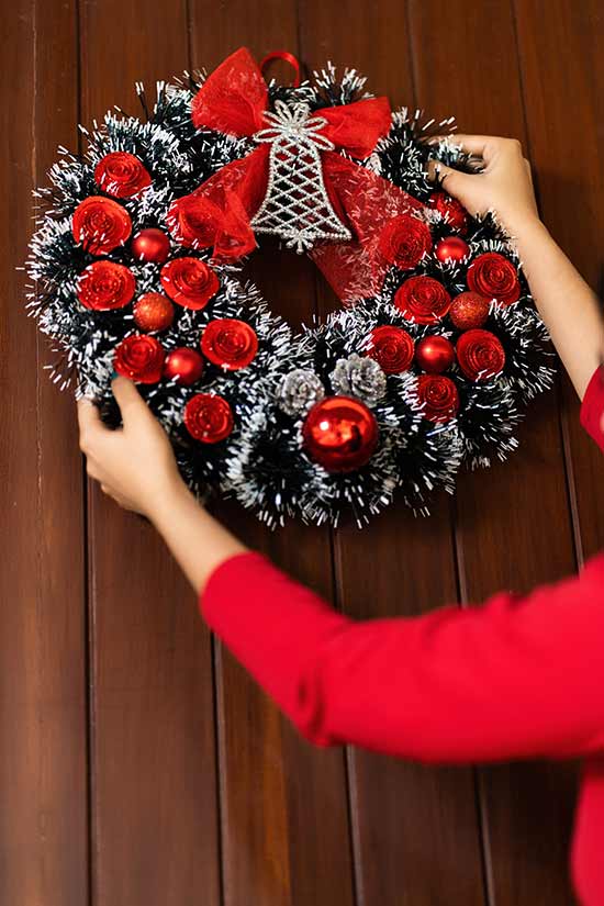 woman hanging up a christmas wreath on a door