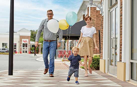 young couple with small child holding balloons walking down a city sidewalk