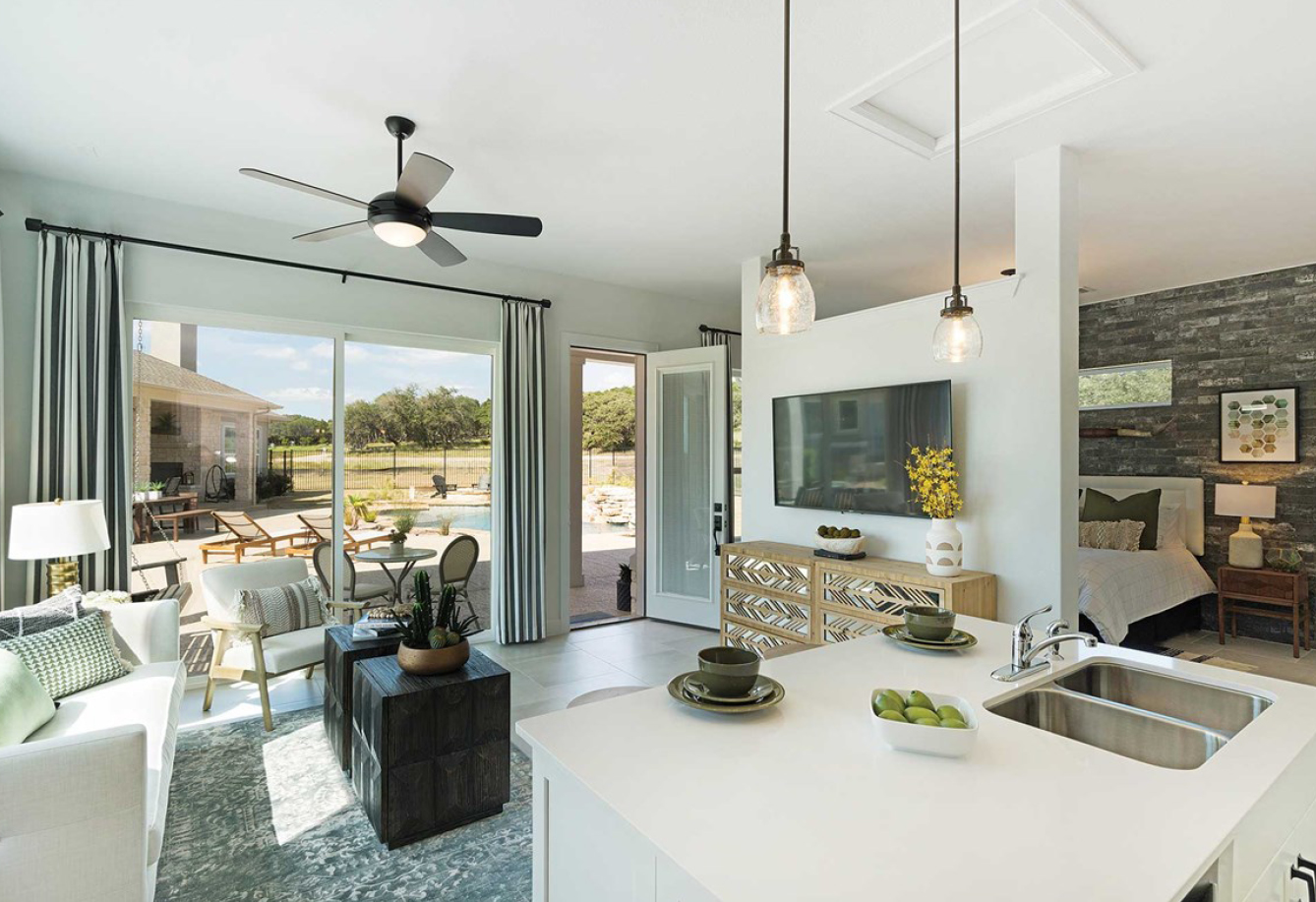 An interior photograph of a David Weekley Homes casita, showing a view from behind the kitchen island that ranges from the living area, windows overlooking a shared backyard view, and the bedroom behind a privacy wall.