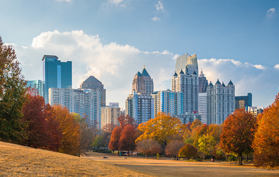 Autumn trees surround an open parkland dotted with Atlanta residents and visitors with the Downtown Atlanta skyline visible in the background