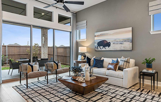 A David Weekley model home’s family room with chairs, a sofa and a coffe table in the foreground and examples of transom windows near the ceiling behind the sofa and above the sliding glass doors.