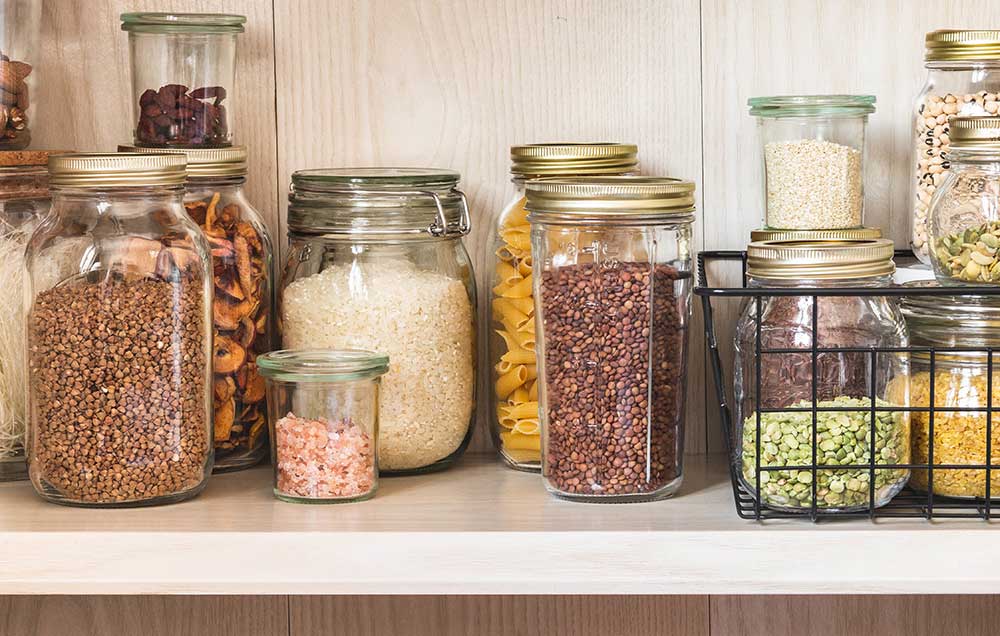 Glass jars full of rice, quinoa, lentils, nuts, dried fruit, beans, noodles, and pink salt.