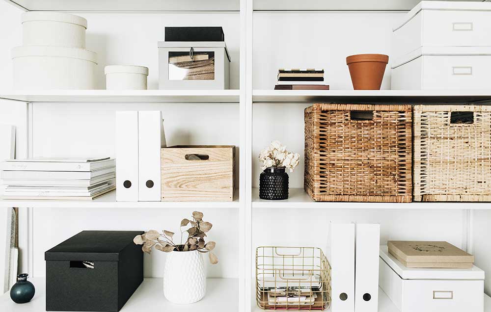 White bookshelves containing a variety of books, baskets, bins, pots and boxes.
