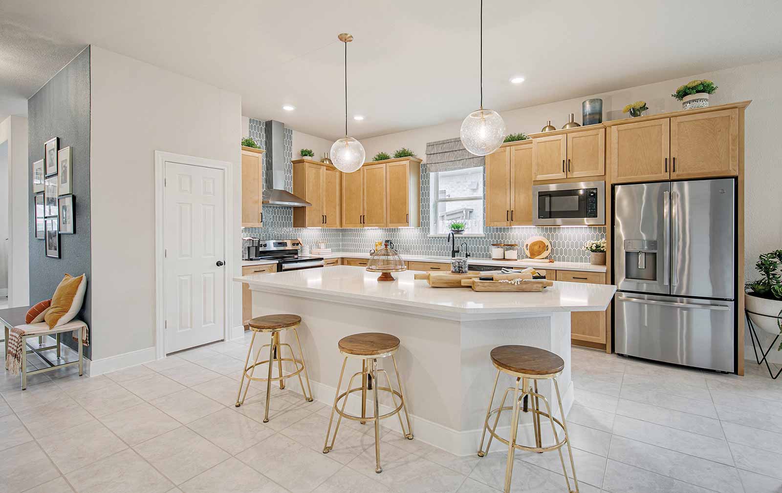 A white island with white quartz countertops rests in the foreground, with tan cabinets and a light blue backsplash behind it. The recessed lighting under the cabinets draw the eye toward decorative flourishes and elegant functional pieces, such as ingredient jars.