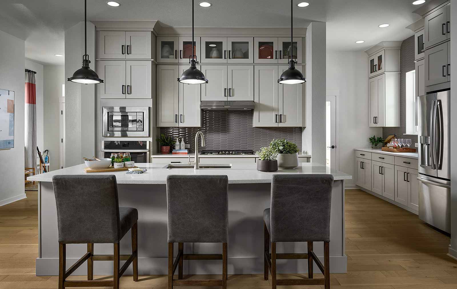 Soft gray carpentry at the island pairs with white quartz  countertops, country-white cabinetry, stainless steel appliances and a soft gray backsplash create a gentle contrast that improves this kitchen’s air of spaciousness.