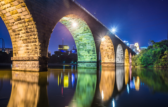 Colorful lights illuminate the arches of the Stone Arch Bridge over the Mississippi River, a sight that impresses many new Minnesotans who relocate to Minneapolis