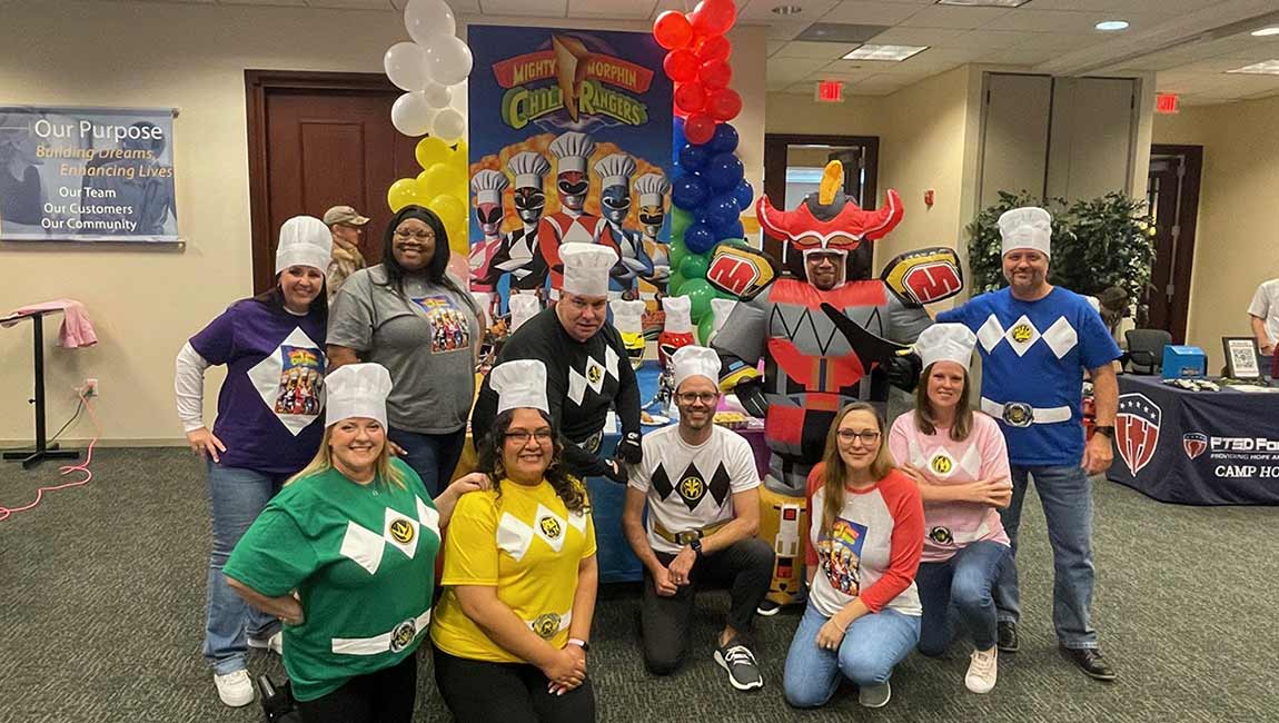 David Weekley Homes Team Members posing in front of a Charity Chili Cookoff display