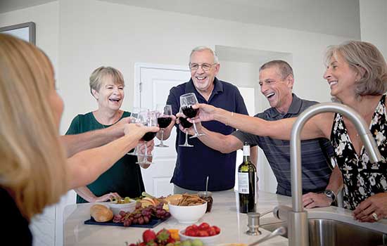 five active adults enjoying glasses of wine in a kitchen